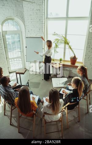 Analyzing. Female speaker giving presentation in hall at workshop. Business centre. Rear view of participants in audience. Conference event, training. Education, diversity, inclusive concept. Stock Photo