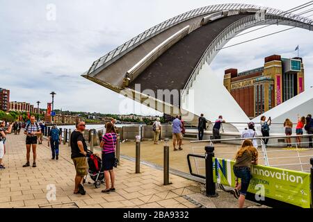 Gateshead Millennium Bridge, a tilt bridge, raised to let boats pass while people wait and watch. Newcastle upon Tyne, UK. August 2018. Stock Photo
