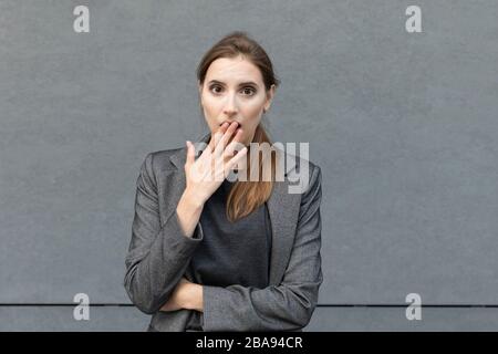 Young beautiful woman is standing in a gray business suit on the background of an office building. The business lady is very surprised, on her face a Stock Photo