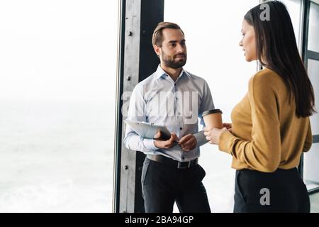 Portrait of young successful colleagues holding papers and discussing business plans while working in office Stock Photo