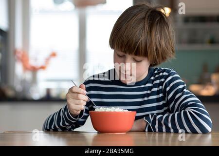 Child eating rice pudding at the kitchen table Stock Photo