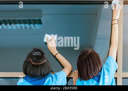 Back view of female students are helping to wipe the glass with wet newspaper at school. Stock Photo