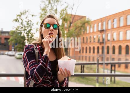 A young girl eats her french fries right on the street. She is very hungry, brutal appetite awoke in her. Stock Photo