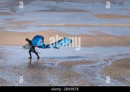 A lone kite boarder surfer struggling to carry his kite boarding surfing equipment in high winds on Fistral Beach in Newquay in Cornwall. Stock Photo