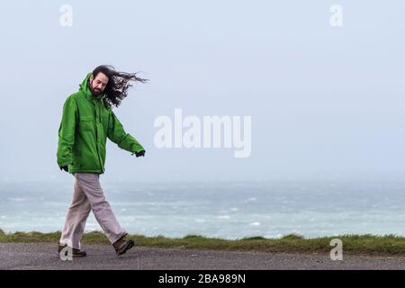 A man with long hair walking in very strong wind.
