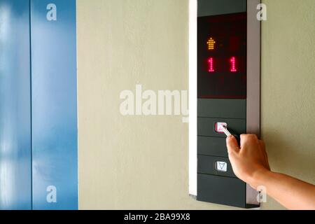 Hand pressing the button of elevator with key for self-sanitization Stock Photo