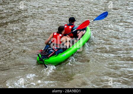 Rear view of two men on a bright green canoe, travelling down the River Thames near the Greenwich Peninsula London, taken on the 18th of August 2019 Stock Photo