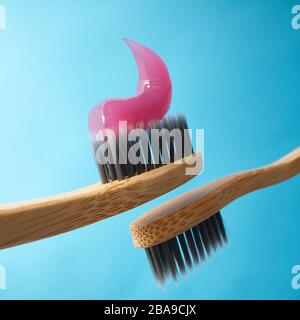 Pink toothpaste on a natural bamboo toothbrush with black charcoal bristles on a blue background Stock Photo