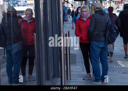 West Norwood, England. 26th March 2020. A woman wearing protective face mask waits outside Iceland supermarket in South London during the coronavirus pandemic. Credit: Sam Mellish / Alamy Live News Stock Photo