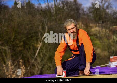 Roof installation. Bearded man work outdoor. Roof Mechanic concept. Inspect repair and replace. Assemble temporary equipment or structures. Structural sheathing. Fix or build. Roofer repair roof. Stock Photo