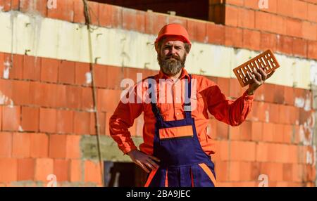 Builder hold brick. Bearded man wear hard hat at construction site. Brick building material used to make walls. Lightweight brick made from expanded clay aggregate. Element in masonry construction. Stock Photo