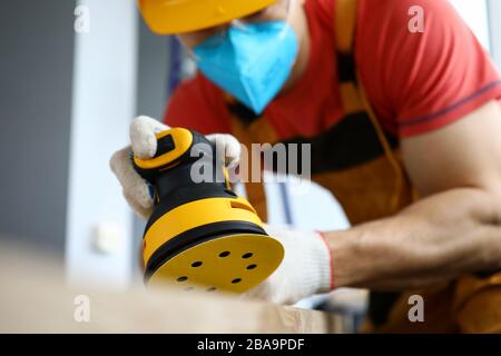 Male construction worker wearing hardhat and protective mask using sanding machine Stock Photo