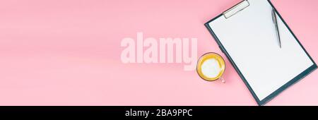 Tablet with a white sheet on which there is a silver pen and next to there is a glass with a coffe with milk Stock Photo