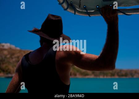 A man in wears an iconic symbol of Australian culture, thinks pensively as he journeys between islands in Western Australia. Stock Photo