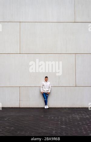 Portrait of young male with hands on pocket leaning on wall outdoors Stock Photo