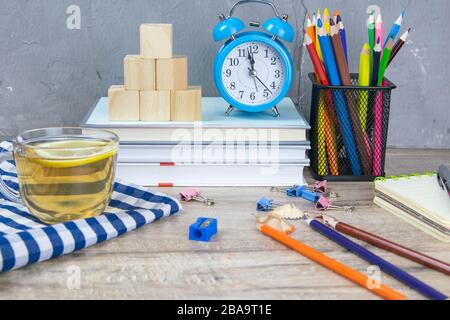 A stack of books, a clock, wooden cubes in the shape of a pyramid, next to there is tea with lemon in a transparent glass glass and multi-colored Stock Photo