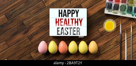 easter eggs with message HAPPY HEALTHY EASTER surrounded by brushes and water color boxes on wooden background Stock Photo