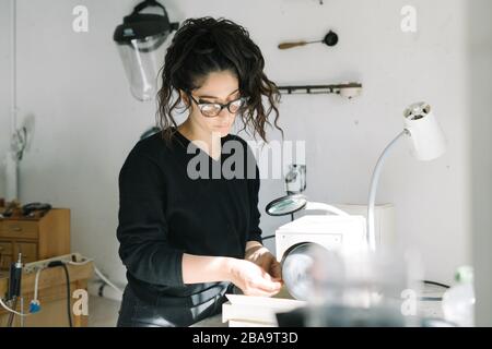 Female artist working with magnifying glass and grinder on jewelry Stock Photo