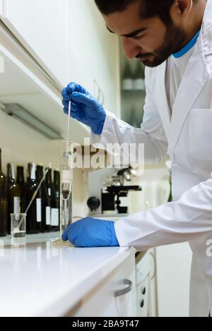 Arabic winemaker working in winelab wearing white gown and gloves. Stock Photo