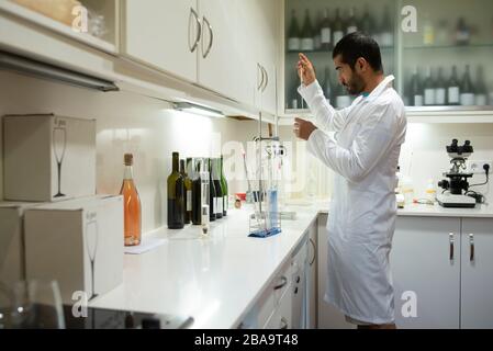 Arabic winemaker working in winelab wearing white gown and gloves. Stock Photo