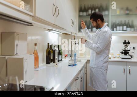 Arabic winemaker working in winelab wearing white gown and gloves. Stock Photo