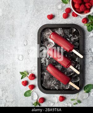 Raspberry popsicles on a tray with ice and fruit on grey background. Stock Photo