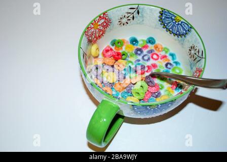 Close up of a bowl full of fruit flavored loops of sugar ready to eat breakfast cereal with a spoon sticking out Stock Photo