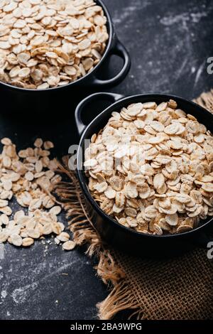 Two black bowls and spoon with raw oatmeal on a black background. Breakfast with fibers for a balanced diet. Oat photo Stock Photo