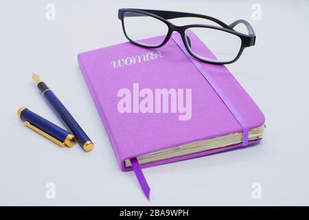 Purple diary for writing of woman with blue and purple pen and black glasses on white background Stock Photo
