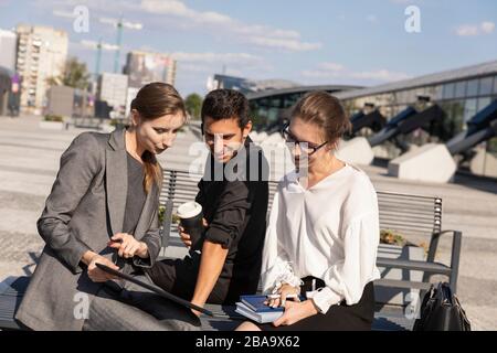 Business partners on the background of an office building. They are sitting on a bench during the lunch break and discussing a future project. Stock Photo