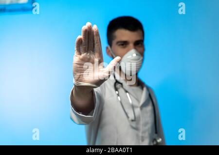 Stop COVID 19 concept. Young doctor in medical uniform with a protective face mask and gloves showing stop hands gesture for stop coronavirus outbreak Stock Photo