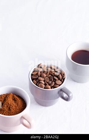Composition from three cups of coffee roasted beans, freshly ground and aromatic fresh brewed drink on a light grey marble background, copy space. Stock Photo