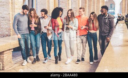 group of interracial friends meeting in the city center. they are having fun with smart phones and social media, walking together and chatting togethe Stock Photo