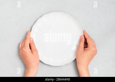 Young woman hands holding white empty plate on neutral concrete background. Image with copy space, top view Stock Photo