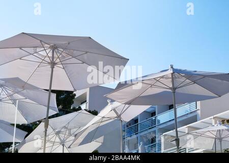 White beach umbrellas, parasols and chaise for relax and comfort on terrace of hotel on sea coast. Happy summer vacations and resort concept. Stock Photo