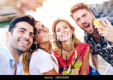Happy friends in the seaside taking selfie in the summer drinking colorful cocktails. Stock Photo