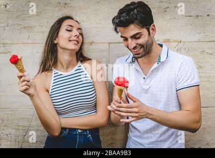 A couple of young lovers flirting and talking eating an Italian gelato against a white wall. Stock Photo