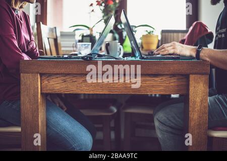 Couple working from home during coronavirus pandemic. Candid image of man and woman sitting at one table with their laptops and other stuff nearby. Stock Photo