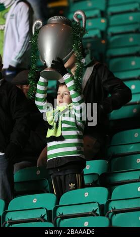 A young Celtic fan holds aloft a champions league trophy in the stands Stock Photo