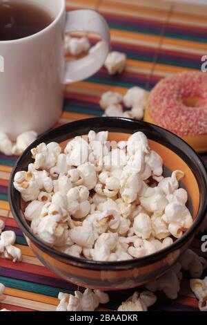 Close up of popcorn in a bowl with tea and donut on table  Stock Photo