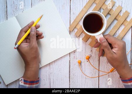 top view of hand writing on notepad, tea on table . Stock Photo