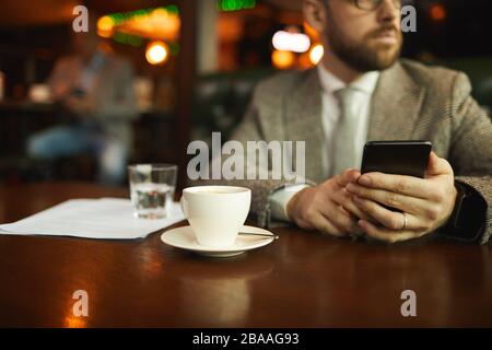 Close-up of young man holding mobile phone while sitting at the table with cup of coffee in cafe Stock Photo