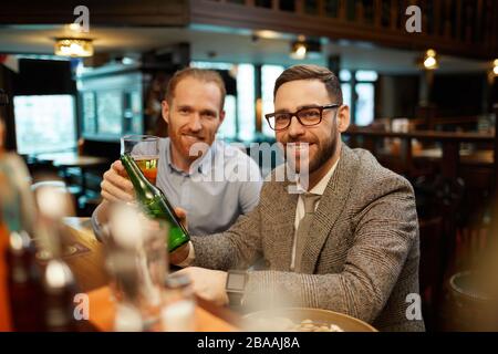 Portrait of two friends smiling at camera while drinking beer at bar counter in the bar Stock Photo