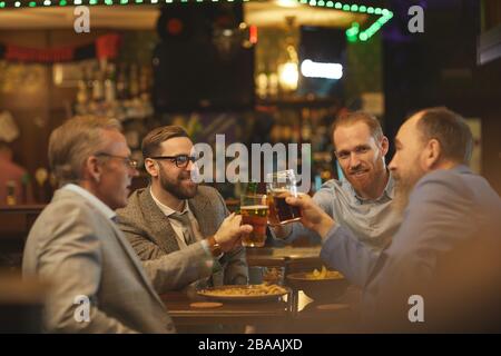 Group of businessmen holding glasses of beer and discussing some working moments in informal setting in the pub Stock Photo