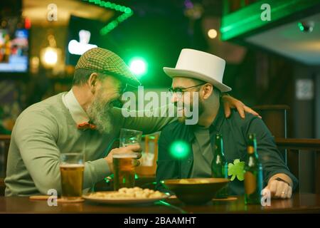 Two bearded men laughing and talking to each other while drinking beer at the table in the pub Stock Photo