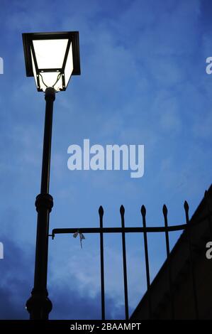 silhouette of Spanish streetlight next to metal bars in night time on a cloudy day Stock Photo