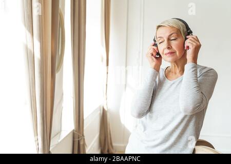 Serene woman in the headphones standing by the window Stock Photo