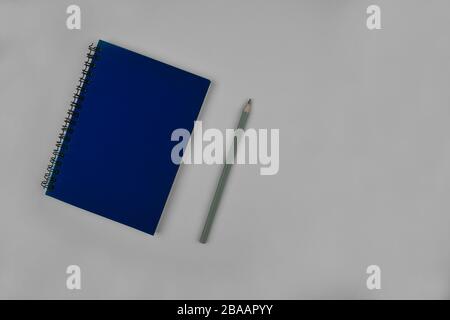 Silver colored wood pencil crayon placed beside a simple blue notebook over a paper background Stock Photo