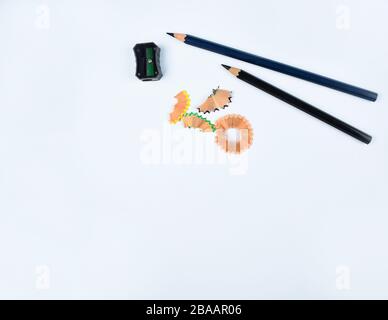 Two black wood pencil,a black pencil sharpener and some pencil shavings scattered on a white background Stock Photo