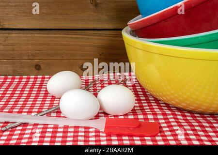 stack of retro mixing bowls on checkered tablecloth with white eggs and kitchen utensils Stock Photo